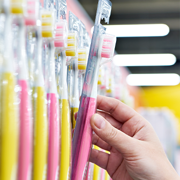 ALFAST® 13 Hand greift nach einer Zahnbürste in einem Supermarktregal, umgeben von zahlreichen weiteren Zahnbürsten in Verpackungen.